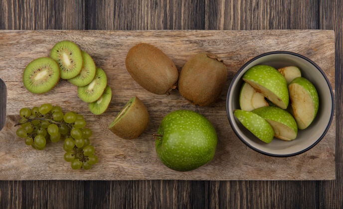 碗顶视图绿色苹果片与猕猴桃片和绿色葡萄在一个木制背景板碗木板苹果切片