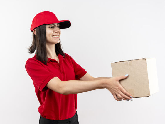 赠送身着红色制服 头戴礼帽的年轻送货员站在白色的墙上 高兴地微笑着向顾客赠送礼盒欢呼帽子微笑
