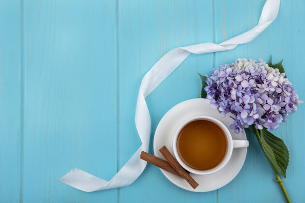 丝带茶杯和肉桂茶托的俯视图 蓝色背景上有鲜花和丝带 还有复制空间桌子肉桂蓝色