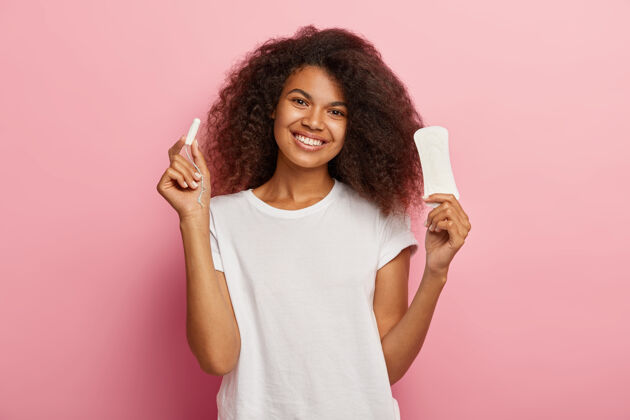 经期快乐年轻非洲女性的孤立镜头拿着尺寸棉条和卫生巾垫护理卫生棉条