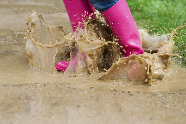 草穿着胶靴的年轻女子跳进了水坑湿滴不卫生