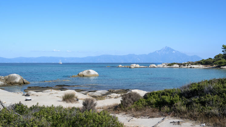 山爱琴海沿岸有游泳的人 水面上有岩石 远处有船 前景是绿色 蓝色的海水 希腊爱琴海沙海岸线