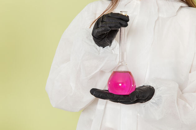 工作前视图穿着特殊防护服的女化学家 手拿淡绿色表面上的粉红色溶液医疗实验室外套