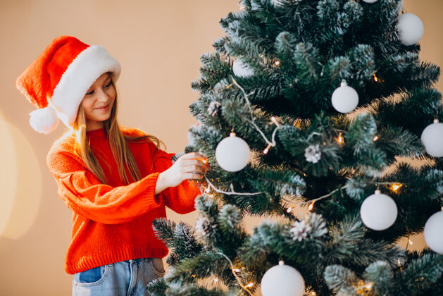 圣诞帽可爱的少女戴着圣诞树旁的红色圣诞帽灯人家