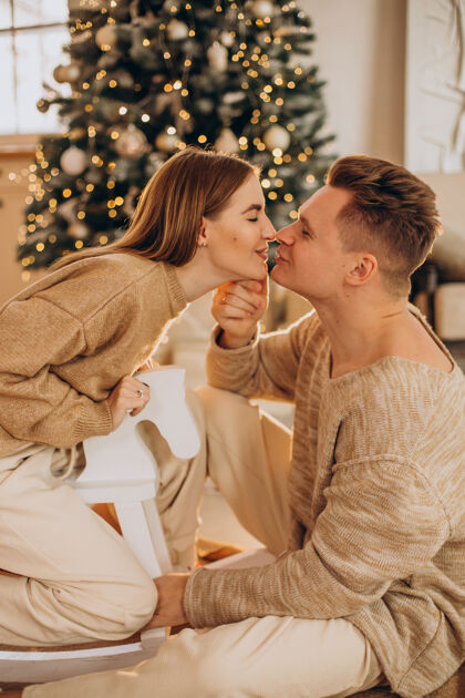 情侣一对年轻夫妇在圣诞树旁互相制作礼物Bokeh圣诞灯圣诞