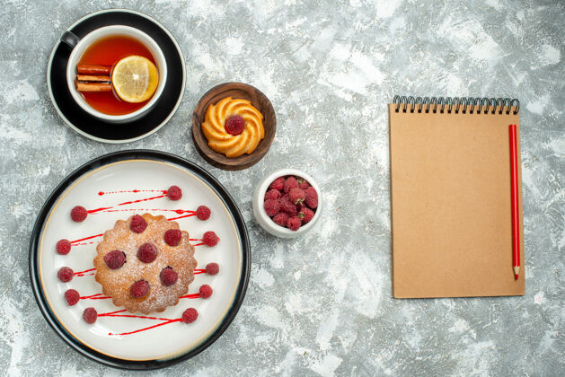 肉桂俯视图一杯茶 柠檬片和肉桂浆果蛋糕放在椭圆形平板笔记本上 灰色表面茶杯盘子盘子
