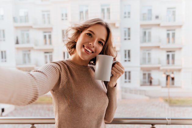 快乐美丽的微笑着的女人 端着一杯咖啡站在城市里积极的黑发女孩 一边喝茶一边享受着早晨室内肖像成人