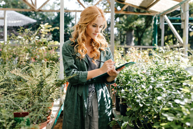 花店一位金发碧眼 笑容温柔的年轻女子 身着绿色长袍 系着腰带 正在温室里工作欢笑植物公园