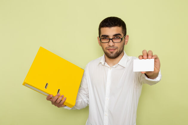 衬衫身穿白衬衫的男办公室工作人员手持卡片 绿色墙上有黄色文件工人男性前面