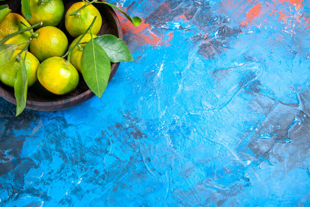 新鲜顶视图黄色橘子与树叶在木制碗蓝色表面与复制空间果汁碗飞溅