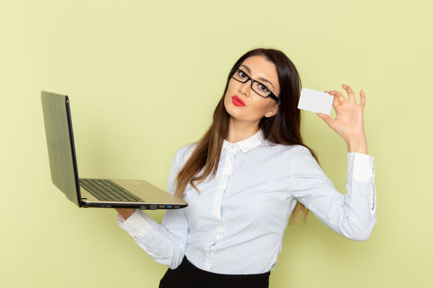 工作穿着白衬衫和黑裙子的女上班族在浅绿色墙上使用笔记本电脑的前视图秘书商务女性漂亮