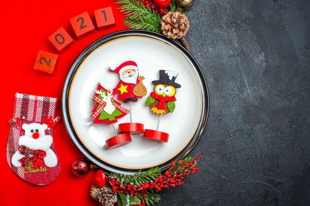 风景新年背景的顶视图 带有餐盘装饰配件杉木树枝和数字圣诞袜 放在黑色桌子上的红色餐巾上冷杉号码圣诞节