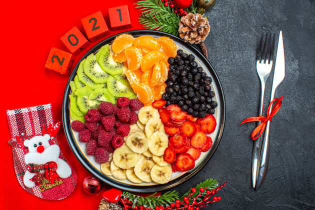 餐盘收集新鲜水果的顶视图 餐盘装饰配件 杉木树枝和数字 红色餐巾上的圣诞袜 黑色背景上的餐具午餐晚餐水果