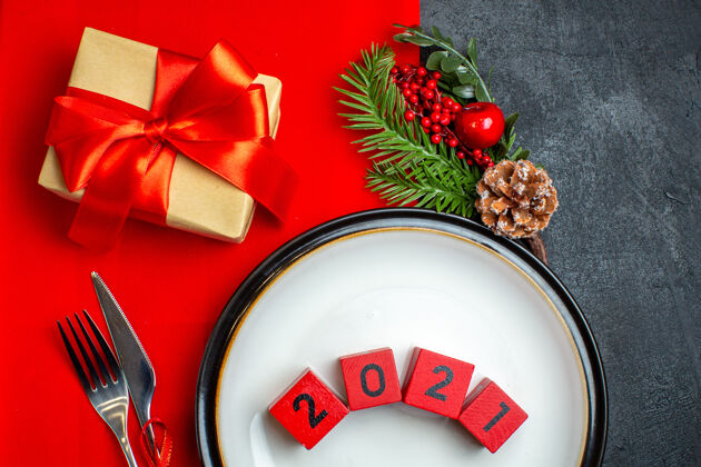 数字上图为新年背景图 餐盘上有数字餐具套装装饰配件杉木树枝旁边有一个红色餐巾上的礼物冬青圣诞餐巾