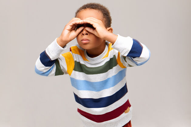 搜索一个好奇的非裔美国男孩用双手靠近眼睛做手势 像用望远镜一样透过洞看 在远处寻找某物的孤立镜头童年和有趣的概念学校儿子小