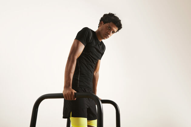 器械严肃的年轻肌肉发达的非裔美国运动员 穿着黑色技术t恤和黑黄相间的短裤 在白色隔离的短横杆上做俯卧撑锻炼肌肉手臂