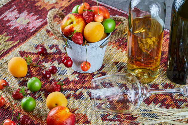 油桃一桶新鲜的夏日水果 一瓶白葡萄酒和一个空杯子 放在雕刻的地毯上杏子草莓酒精