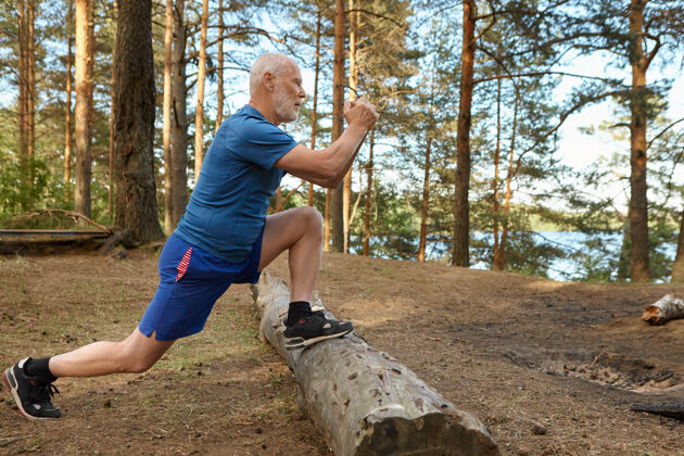 运动装强身健体 留胡须的老年男子在森林里锻炼身体 弓箭步 脚踩木头的侧视图阳光明媚的夏日 老年男子集中精力锻炼腿部肌肉森林脚追求
