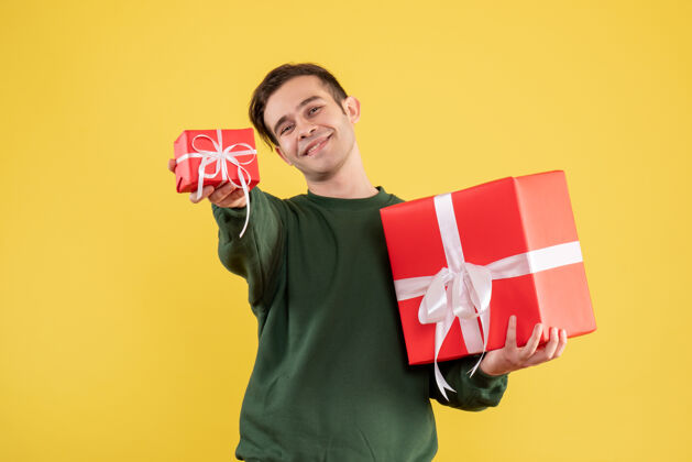 年轻人正面图穿绿色毛衣的年轻人站在黄色的椅子上送圣诞礼物购物持有微笑