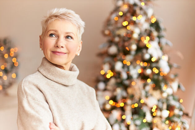 室内节日 传统和庆祝的概念迷人的60岁妇女穿着舒适的毛衣站在客厅装饰着宏伟的圣诞树与装饰品 花环和灯圣诞节庆祝微笑