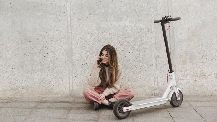 电话一个年轻的女人和一辆电动滑板车摆姿势交通电动滑板车城市交通