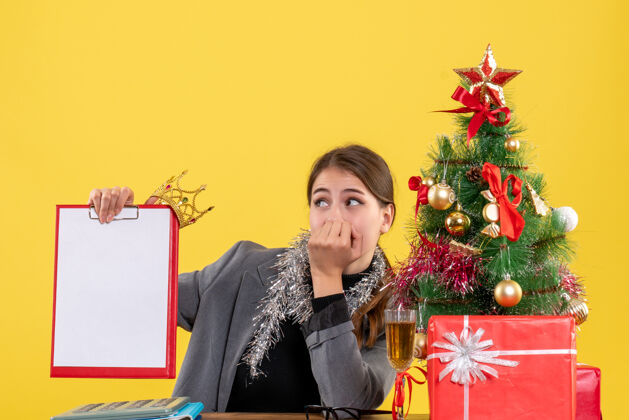 流浪前视图漫步的女孩坐在桌子旁拿着文件 头戴圣诞树和鸡尾酒礼物圣诞节笔记本电脑人