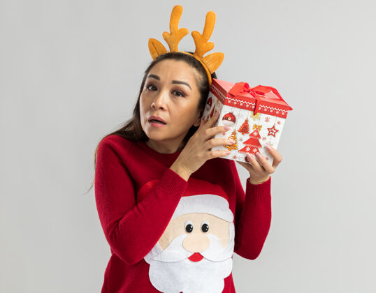 耳朵穿着红色圣诞毛衣的年轻女子 戴着滑稽的鹿角边 耳朵上挂着圣诞礼物 想听听什么礼物边年