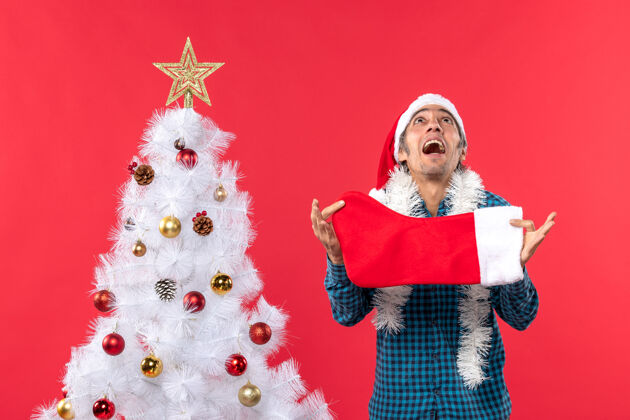 圣诞情绪激动的年轻人戴着圣诞老人的帽子 穿着蓝色的衬衫 手里拿着圣诞袜子 往上看帽子圣诞老人庆祝