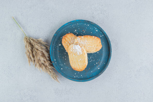 糕点蓝色盘子上的片状饼干 旁边是大理石背景上的一根羽毛草甜点美味美味