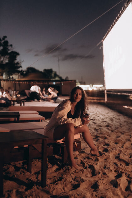 坐着年轻女子坐在夜滩的椅子上 看着摄像机女人女性热带