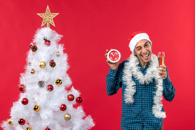 站着一个带着圣诞老人帽子 拿着一杯酒 站着闹钟的疯狂的情绪化的年轻人圣诞老人圣诞疯狂
