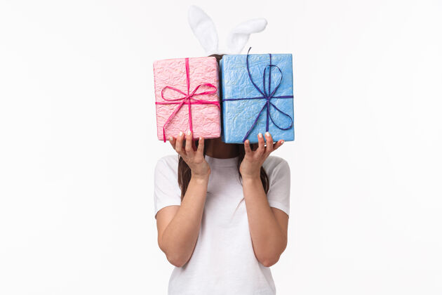 复活节可爱的复活节兔女在兔子耳朵 隐藏在粉彩包装礼品盒后面她的脸庆祝女人折扣