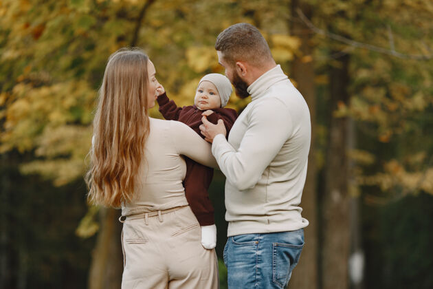 公园秋天公园里的一家人穿棕色毛衣的男人和父母在一起的可爱小女孩成人孩子户外
