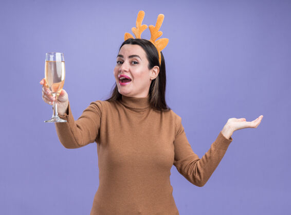 篮球兴奋的年轻漂亮女孩穿着棕色毛衣 戴着圣诞发箍 手拿香槟杯 手被隔离在蓝色的墙上毛衣圣诞节年轻