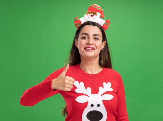 篮球微笑着的年轻漂亮女孩穿着圣诞毛衣 戴着圣诞发箍 在绿色的背景上孤立地竖起大拇指女孩拇指微笑