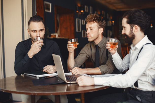 分析谈判中的商人坐在桌边喝酒的男人朋友们在聊天经理当代人合作伙伴