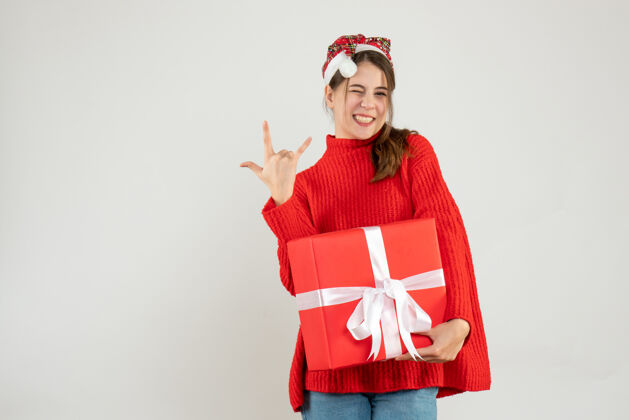 购物戴着圣诞帽的快乐女孩在白色的石头上拿着礼物举行圣诞节女孩