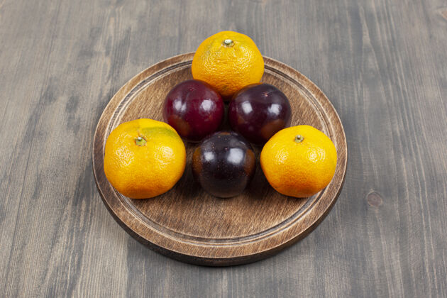 水果美味的李子和美味的橘子放在木盘上高品质的照片柑橘碗木料