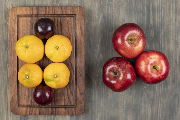 健康多汁的红苹果 李子和橘子放在木砧板上高质量的照片成熟甜味食物