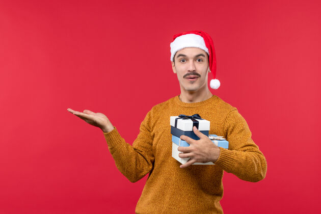 光带着礼物的年轻人在浅红色墙上的正视图可爱年轻男性圣诞节