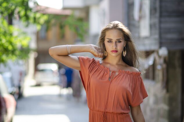 模特在一个背景模糊的小巷里 一个穿着红橙色裙子的女模特的选择性聚焦镜头胡同美女化妆