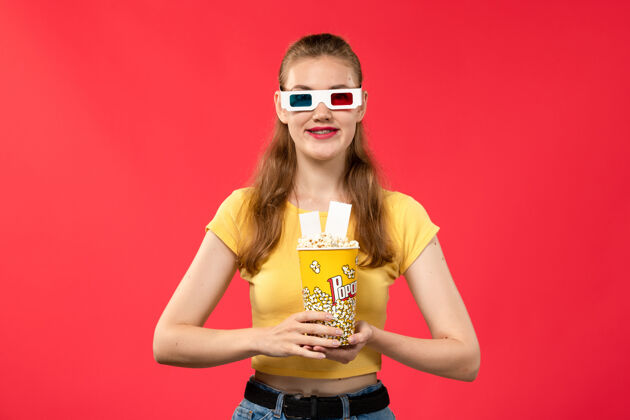 漂亮前视图年轻的女性在电影院拿着爆米花包在-d太阳镜在浅红色的墙壁影院电影女性爆米花成人