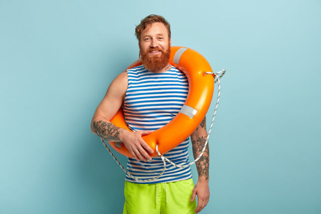 设备快乐的红发男性度假者穿着水手背心和短裤 带着橙色救生圈在海里游泳安全狐狸胡须