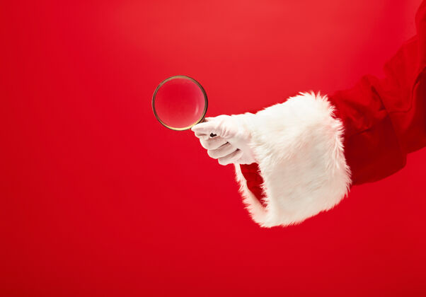 结圣诞老人的手拿着放大镜在红色的夏娃圣诞老人放大镜