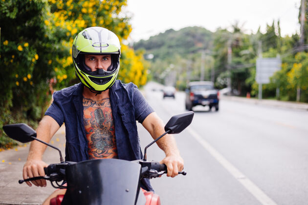 自由在泰国繁忙的公路边 骑摩托车的戴着黄色头盔的男性纹身车手的肖像人夏天街道
