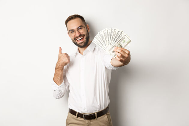 脸成功的商人展示金钱美元和竖起大拇指 微笑满意 站着成功雇员收入