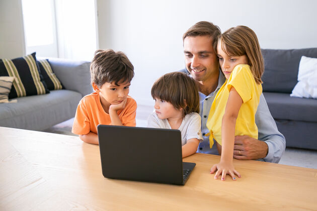 可爱快乐的爸爸坐在餐桌旁 拥抱孩子 使用笔记本电脑高加索中年爸爸和可爱的孩子一起上网童年 父爱和数字技术概念童年可爱男孩