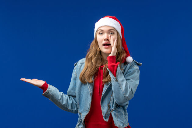 人物前视图年轻女性在红色圣诞帽上的蓝色背景圣诞情感色彩表演者成人圣诞节