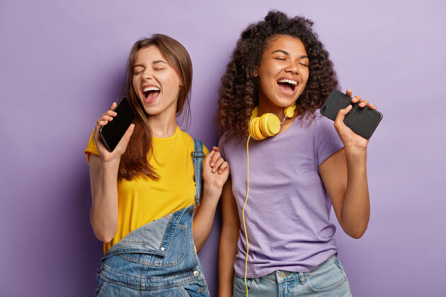 多样化乐观快乐的混血女性用智能手机唱最喜欢的歌 尽情享受音乐 闭上眼睛 积极行动混合在一起非洲