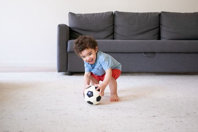 站立快乐的小男孩在家玩足球 微笑着可爱的婴儿赤脚站在地毯上 在客厅里玩得很开心假期 周末和童年的概念新生儿游戏孩子